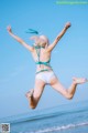 A woman in a bikini jumping in the air on the beach.